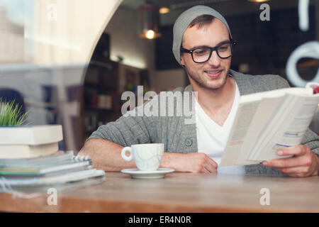 Lächelnd Hipster Mann Lesebuch im Café. Krakau, Polen Stockfoto