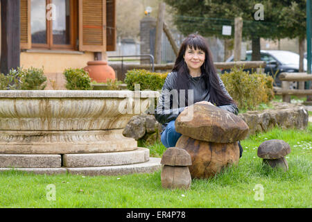 Ein Mädchen posiert und lächelnd hinter einem Holz Pilz Stockfoto