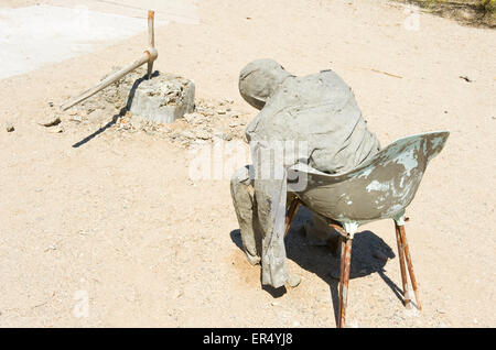 Mannequin in saß im Stuhl aus Kunststoff, Zement bedeckt Spitzhacke im Hintergrund, Kunstwerk, Ost Niland Jesus, Slab City, Kalifornien. Stockfoto