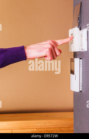 Junge männliche Hand Drücken der Taste der elektronische Thermostat an Wand des modernen Hauses. Sauberer Hintergrund Szene lila Wollpullover. Stockfoto