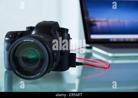 Stillleben mit Dslr-Kamera mit USB-Kabel an Laptop-Computer auf Glastisch verbunden. Die Foto-Kamera überträgt Bilder Stockfoto