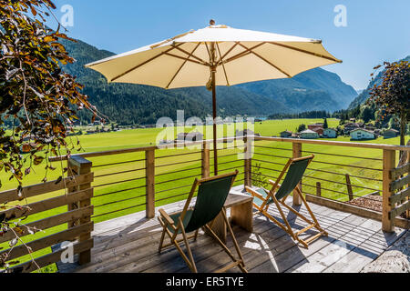 Liegestühle und Sonnenschirm auf der Terrasse, See Achensee und Achenkirch im Hintergrund, Tirol, Österreich Stockfoto