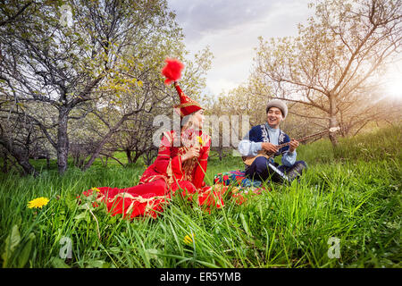 Kasachische Mann Dombura spielen und singen das Lied für die Frau in rot auf dem grünen Rasen in Almaty, Kasachstan, Zentralasien Stockfoto