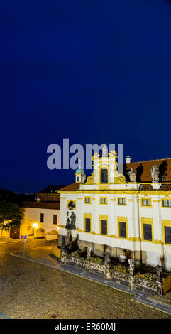 Nachtansicht der Fassade der Loreta Kirche in Prag: grünes Dach auf weißen Glockenturm, weiße Wände, rote auf dem Dach. Stockfoto