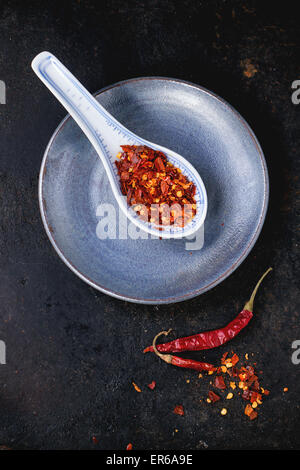 Sortiment an ganze getrocknet und Flocken Rot-heiße Paprika in Keramik Löffel auf schwarzem Hintergrund Stockfoto