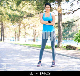 In voller Länge Portrait einer Fitness hübsche Frau stand mit verschränkten Armen im Freien im Park und Blick in die Kamera Stockfoto