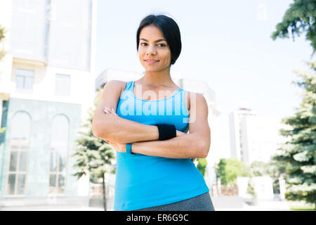 Sportliche Frau mit Armen im Freien mit dem Aufbau auf Hintergrund und Blick in die Kamera Stockfoto