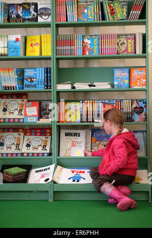 Hay Festival, Powys, Wales - Mai 2015 - Ein junges Mädchen schaut sich eine Auswahl von Büchern in der Kinderabteilung des Hay Festival Buchladens an Stockfoto