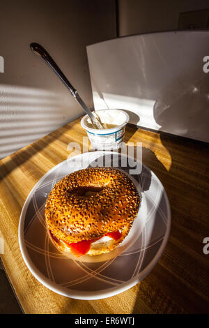 Ein Sesam Samen Bagel mit Frischkäse und Räucherlachs im frühen Morgenlicht streaming über ein Fenster. Stockfoto