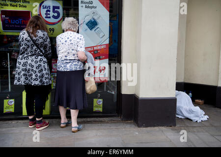 Der Strand. Zwei Frauen suchen im Fenster Rymans Stationers, während ein Obdachloser in einem nahe gelegenen Eingang schläft. Stockfoto