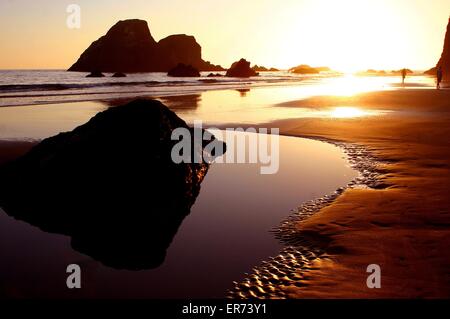 Die Menschen gehen unten am Strand bei Sonnenuntergang über Meer-Stacks auf Trinidad Bay in California Coastal National Monument in Kalifornien. Das Denkmal besteht aus mehr als 20.000 Inselchen, Felsen, Riffe ausgesetzt und Zinnen erstreckt sich die Länge des Staates zwischen Mexiko und Oregon. Stockfoto