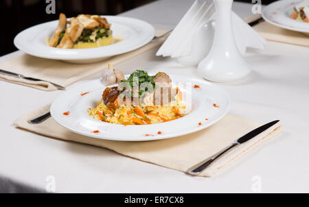 Zubereiteten Speisen in weißen Schalen auf einfache individuelle Gedecke am Tisch im Restaurant serviert Stockfoto