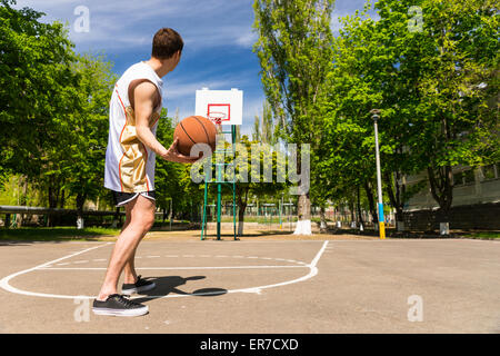 Rückansicht des athletischen jungen Mann kostenlose Basketball von oben Taste auf Freiplatz im üppigen Grün Gericht wirft Stockfoto