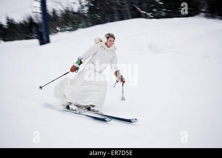 Eine Frau Ski einen Berg hinunter in ein Brautkleid nach der Hochzeit. Stockfoto