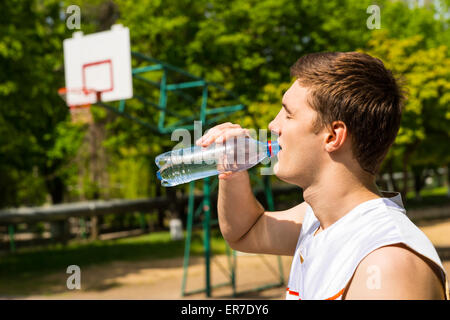 Kopf und Schultern Blick des jungen Mannes Trinkwasser aus der Flasche, eine Pause für Erfrischung und Flüssigkeitszufuhr auf Basketball Cour Stockfoto