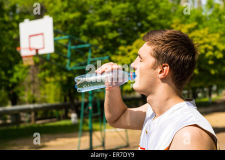 Kopf und Schultern Blick des jungen Mannes Trinkwasser aus der Flasche, eine Pause für Erfrischung und Flüssigkeitszufuhr am Basketballplatz. Stockfoto