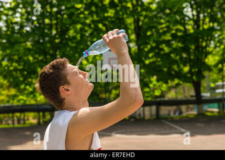 Kopf und Schultern Blick auf jungen sportlichen Mann gießt Wasser aus der Flasche ins Gesicht, eine Pause für Erfrischung und Flüssigkeitszufuhr Stockfoto
