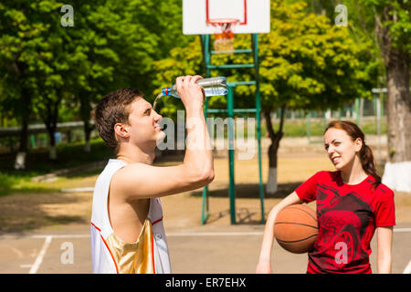 Junge sportliche paar unter einem erfrischenden brechen am Basketballplatz, Frau auf der Suche auf, wie Man die Flasche Wasser ins Gesicht leert Stockfoto