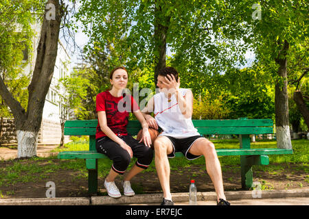 Porträt des jungen Mann und Frau tragen sportliche Kleidung sitzt auf grünen Parkbank mit Basketball dazwischen, wobei eine Bre Stockfoto