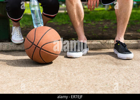 Niedrigen Winkel nahe Ansicht der Basketball auf Boden zu Füßen der sportliche Brautpaar auf Parkbank sitzen nach dem Spiel Stockfoto