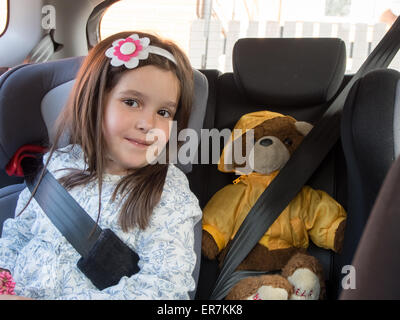 Ein junges Mädchen in einem Auto-Kindersitz mit ihren Teddy in den Sitz neben ihr geschnallt. Stockfoto