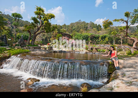 Frau sitzt an einem Wasserfall an einem kleinen Teich im Norden Thailands Stockfoto