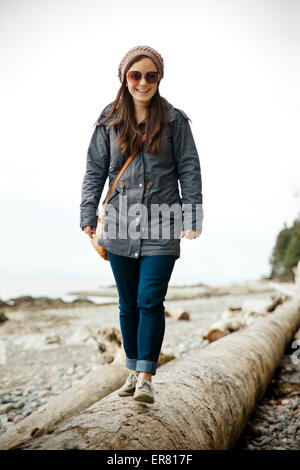 Eine junge Frau geht auf einen langen Baumstamm am Strand in BC, Kanada. Stockfoto