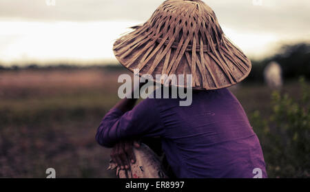 Rückansicht der Frau in Bambushut sitzen auf Feld, Bago Region, Myanmar Stockfoto