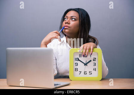 Nachdenklich afroamerikanischen Geschäftsfrau sitzen am Tisch mit Stift und Laprop im Büro über grauen Hintergrund Stockfoto