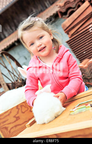 kleines Mädchen mit einem Kaninchen vor dem Bauernhof Stockfoto