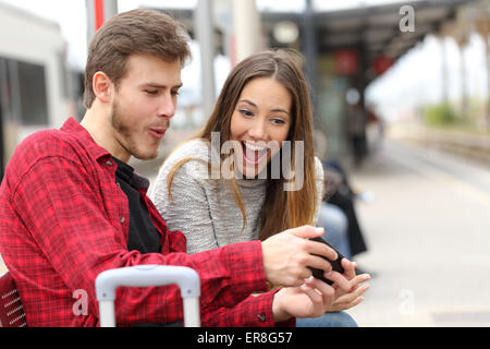 Lustige Spiele mit einem Smartphone in einem Bahnhof, während sie warten paar Stockfoto