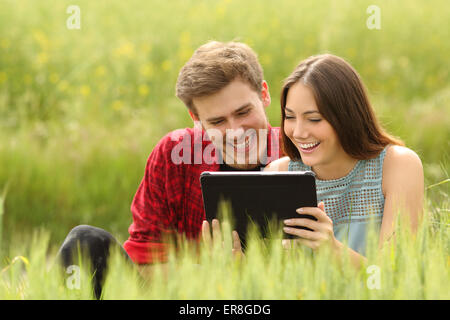 Lustige paar beobachten und Freigabe von Videos in einer Tablette in einem grünen Feld Stockfoto