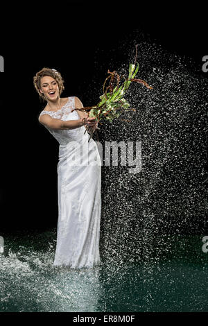 Begeistert junge Braut Spritzwasser mit Bouquet auf schwarzem Hintergrund Stockfoto