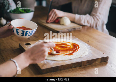 Bild der Frau Tomatensoße über Pizzateig verteilen beschnitten Stockfoto