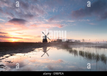 Windmühle durch Fluss im morgendlichen Nebel bei Sonnenaufgang, Niederlande Stockfoto