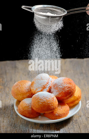 gießt Zucker mit Sieb über donuts Stockfoto