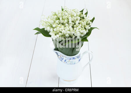Schöner Blumenstrauß Maiglöckchen in weißem Krug auf weißen lackierten Holztisch Stockfoto