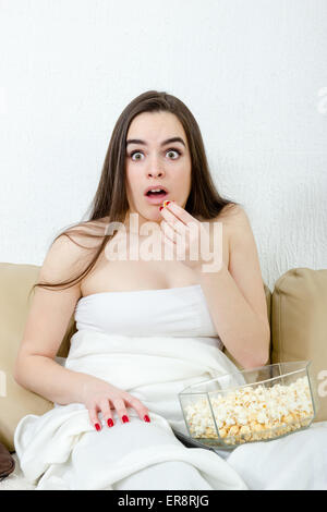 Frau Angst lustig beängstigend Film Popcorn zu essen. Schöne Mädchen vor dem Fernseher im Bett auf weißem Hintergrund inländischen. Schockiert Stockfoto