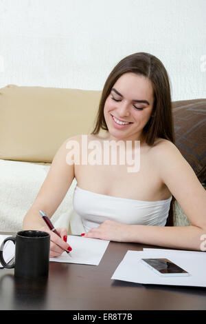 Freizeit und Wohnkonzept - schreibt ruhig Teenager-Mädchen Frau mit Stift auf weißem Papier und sitzen auf der Couch zu Hause. Lächelnde Frau m Stockfoto