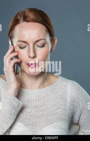 Reife Frau mit Handy vor grauem Hintergrund betont Stockfoto