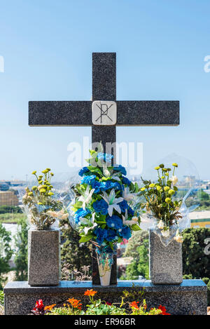 Marmorkreuz mit Blumensträußen gegen blauen Himmel auf einem Friedhof. Stockfoto