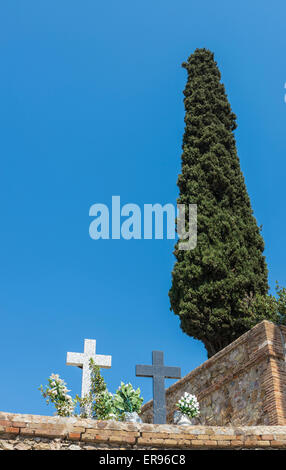 Zwei Marmor kreuzt mit Sträußen und eine Zypresse gegen blauen Himmel auf einem Friedhof Stockfoto