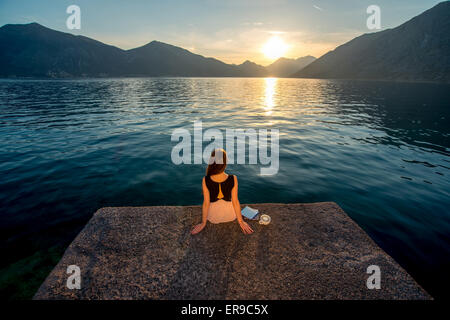 Frau sitzt auf dem Pier bei Sonnenaufgang Stockfoto