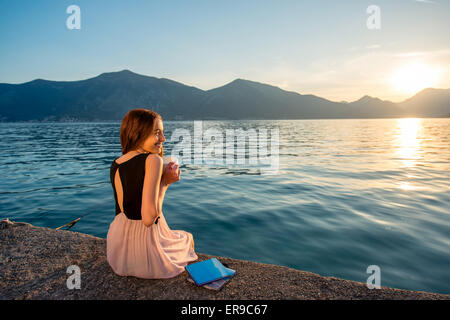 Junge Frau sitzt auf dem Pier bei Sonnenaufgang Stockfoto