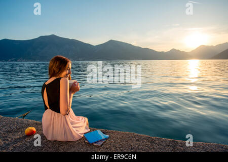 Junge Frau sitzt auf dem Pier bei Sonnenaufgang Stockfoto