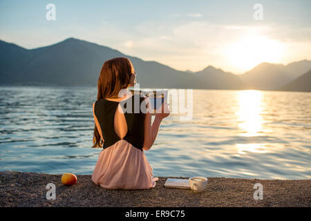 Junge Frau sitzt auf dem Pier bei Sonnenaufgang Stockfoto