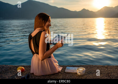 Junge Frau sitzt auf dem Pier bei Sonnenaufgang Stockfoto