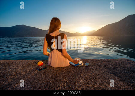 Junge Frau sitzt auf dem Pier bei Sonnenaufgang Stockfoto