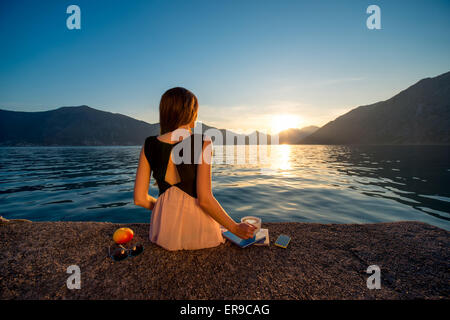 Junge Frau sitzt auf dem Pier bei Sonnenaufgang Stockfoto