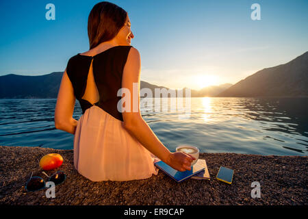 Junge Frau sitzt auf dem Pier bei Sonnenaufgang Stockfoto